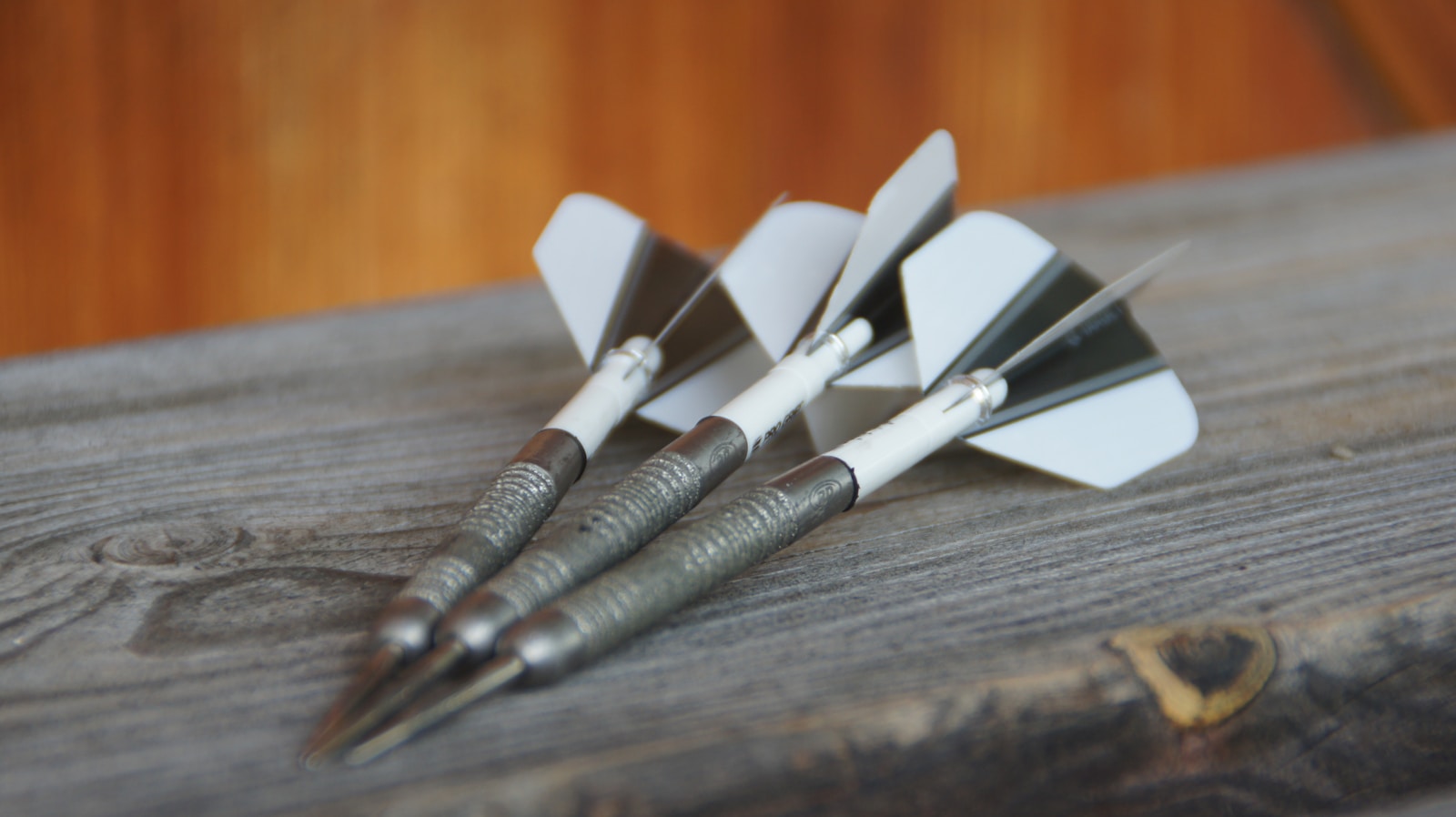 A close up of three metal darts on a wooden surface